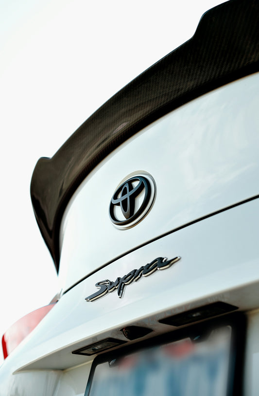 A white toyota supra features a sleek spoiler.